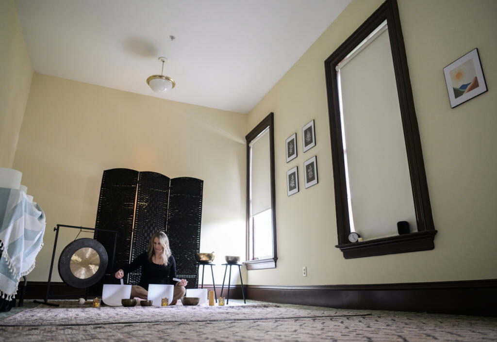 Andrea Kintzley demonstrates crystal singing bowls on March 10 at Soul Space Wellness in the O.O. Howard House. She has a set of several bowls of different sizes, as well as metal and glass bowls, a gong, chimes and rattles and a crystal &ldquo;singing pyramid.&rdquo; (Taylor Balkom/The Columbian)