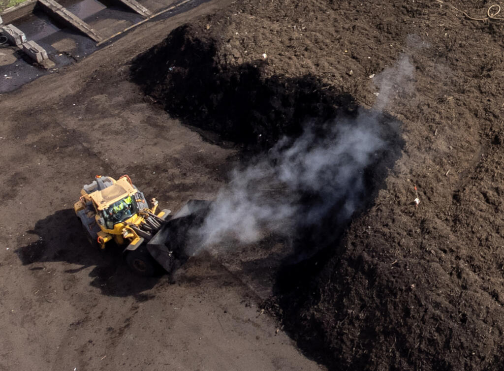 Steam rises from a pile of compost material as a front loader works Friday at the Dirt Hugger composting facility in Dallesport. (Photos by taylor balkom/The Columbian)