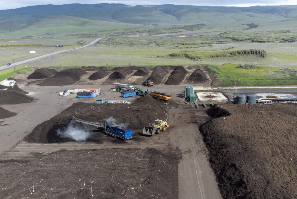 A green landscape sits behind the Dirt Hugger composting facility March 20 in Dallesport. The company uses yard and food waste from Vancouver and Ridgefield to create compost sold at nurseries and landscape supply stores in Clark County. At top, Dirt Hugger co-founder Pierce Louis clumps together a handful of compost. (Taylor Balkom/The Columbian)