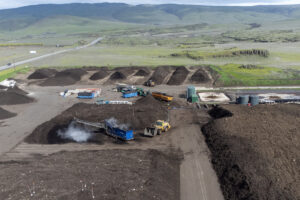A green landscape sits behind the Dirt Hugger composting facility March 20 in Dallesport. The company uses yard and food waste from Vancouver and Ridgefield to create compost sold at nurseries and landscape supply stores in Clark County. At top, Dirt Hugger co-founder Pierce Louis clumps together a handful of compost. (Taylor Balkom/The Columbian)
