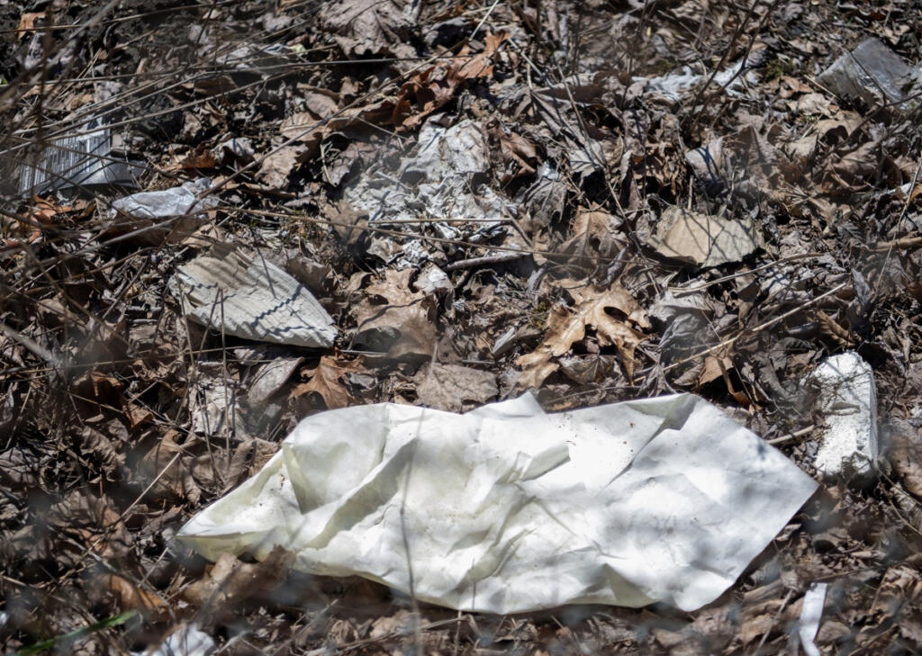 Litter sits among dead leaves March 27 along state Highway 14. (Taylor Balkom/The Columbian)