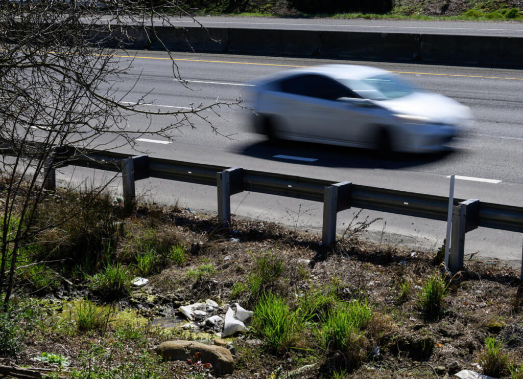 A car zooms by an area where litter has collected March 27 along state Highway 14. (taylor balkom/The Columbian)