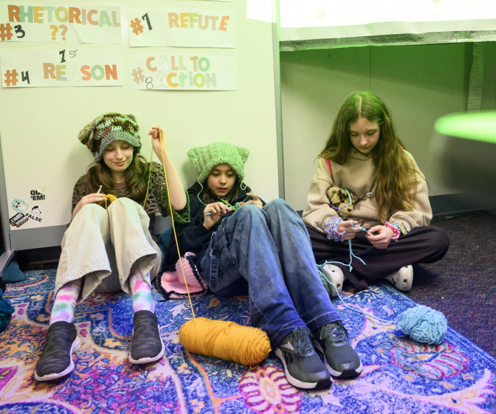 Sixth-graders Sophia Goulding, from left, Morgan Brumbaugh and Avery Baxter sit on the floor and crochet during a crochet club meeting at Pacific Middle School. The crochet craze has spread around the school and some teachers even allow crocheting in class. (Taylor Balkom/The Columbian)