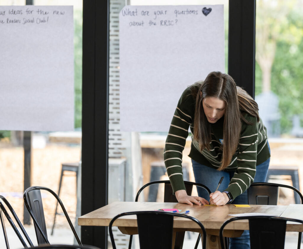 Melanie Clarke of Battle Ground writes an answer to a prompt on a sticky note April 1, 2026, before a Romance Readers Social Club meeting at Ashwood Taps and Trucks in Washougal. (Taylor Balkom/The Columbian)