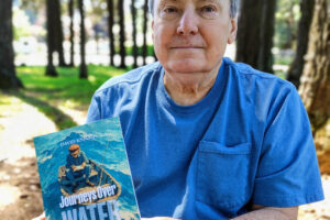 Washougal resident David Knight holds a copy of his memoir, &ldquo;Journeys Over Water,&rdquo; on May 4 at Hathaway Park in Washougal. (Doug Flanagan/The Columbian)