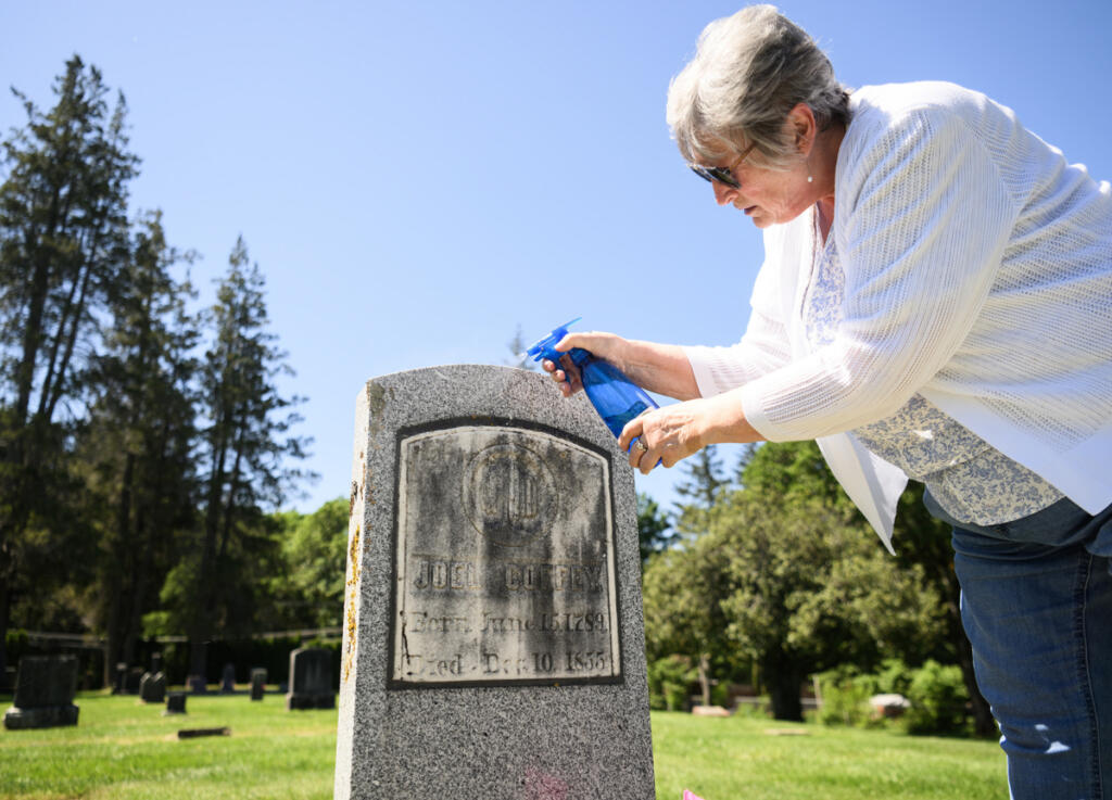 Local historian Peri Muhich cleans the headstone of Joel Coffey, the first person buried at Fern Prairie Cemetery on Monday in Camas. Muhich is leading the Two River Heritage Museum&rsquo;s first tour of the cemetery on  Sunday. (Taylor Balkom/The Columbian)