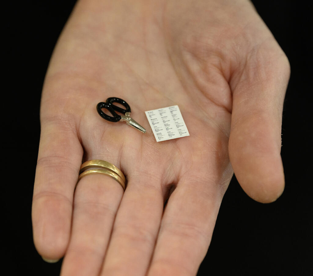 Mini-gallery curator Lara Blair holds a tiny pair of scissors (yes, they actually work) and a tiny card listing participating artists. (Taylor Balkom/The Columbian)
