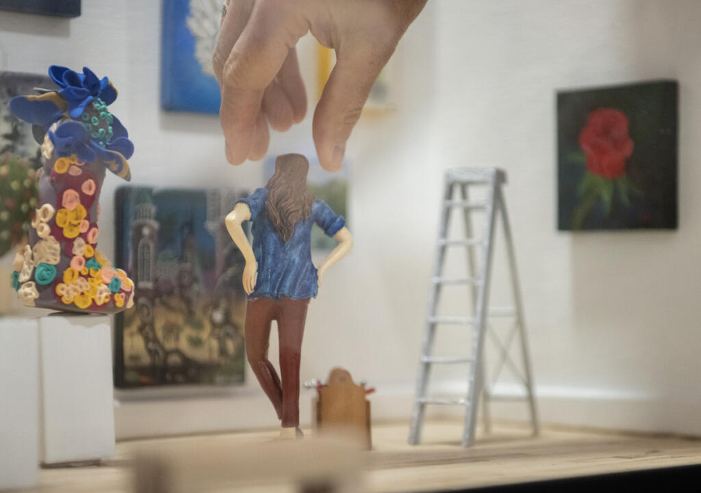 Miniaturist Lara Blair places a tiny figurine inside the Gallery 408 mini-gallery on Wednesday. The mini-gallery will be displayed inside the front window of the larger gallery where passersby can see it. (Taylor Balkom/The Columbian)