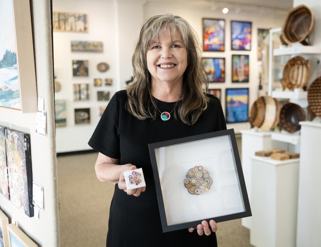 Gallery 408 co-owner Kim Nickens holds two of her intricate paper art pieces. The teensy artwork on the left will hang in her new mini-gallery, which will be officially &ldquo;opened&rdquo; with a ribbon-cutting attended by the mayor of Camas at 5 p.m. June 5, complete with tiny scissors and tiny ribbon. (Taylor Balkom/The Columbian)