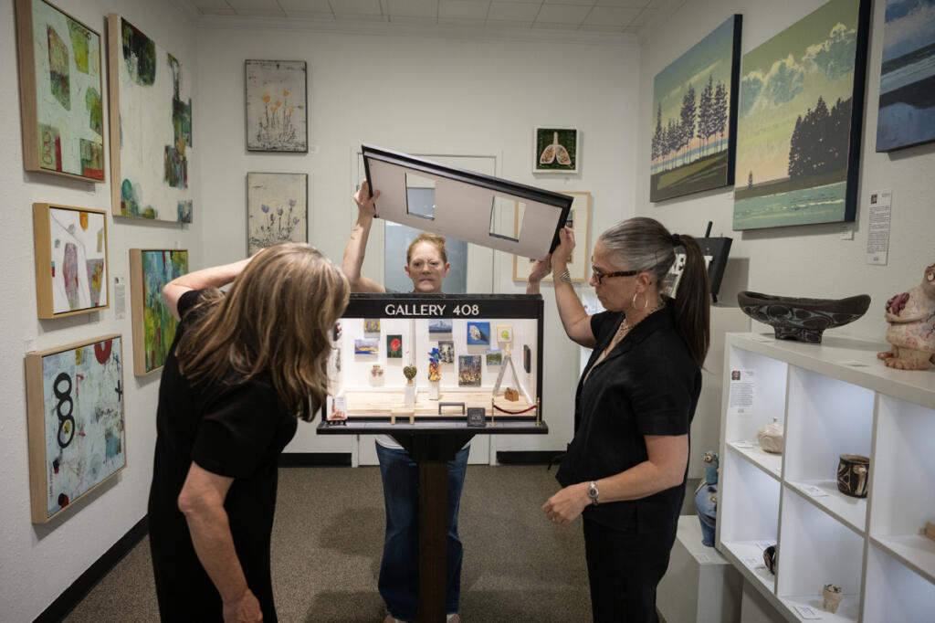 Gallery 408 co-owner Kim Nickens, from left, co-owner Michelle Purvis and curator Lara Blair remove the roof of a miniature art gallery Wednesday at Gallery 408 in Camas. The teensy gallery, designed by Blair and constructed by the gallery co-owners&rsquo; husbands, will become part of the Worldwide Sidewalk Joy Project, which celebrates miniature art installations around the world. The mini-gallery will officially &ldquo;open&rdquo; with a ribbon-cutting ceremony June 5. (Taylor Balkom/The Columbian)