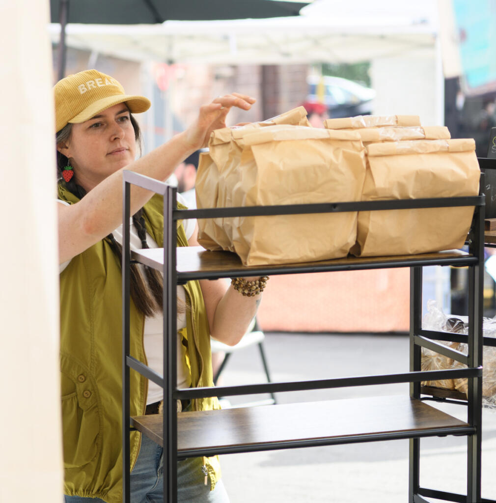 Bakehouse Sourdough owner Kendra Hofseth arranges loaves of bread June 3 at the Camas Farmers Market. (Taylor Balkom/The Columbian)