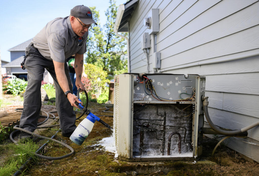 All Seasons Heating and Cooling service manager Ken Sullivan sprays cleaning solution on an air conditioner Friday in Camas. (Taylor Balkom/The Columbian)