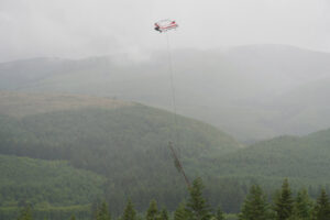A helicopter flies along the South Fork Toutle River valley to carry a large log to the Lower Columbia Fish Enhancement Group&rsquo;s salmon habitat-restoration project. The group has placed hundreds of logs in and along the South Fork Toutle River in recent years. (Contributed by the Lower Columbia Fish Enhancement Group)