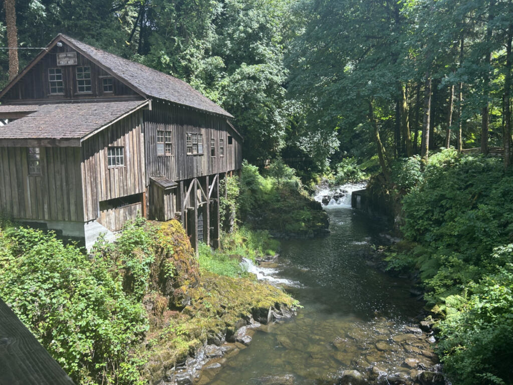 The historic Cedar Creek Grist Mill in Woodland is seen from a nearby covered bridge Saturday afternoon. The mill&rsquo;s main roof, as well as the cedar shake roof on the smaller blacksmith shop seen in the foreground, are in need of repair. (Kelly Moyer/The Columbian)