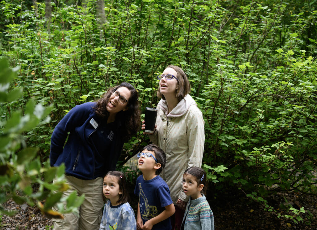 Water Resources Education Center&rsquo;s Suzanne Herbert, from left, helps Cora Eakin, 4, Atlas Eakin, 5, mom Royce Andrews and Penelope Eakin, 4, spot a birds nest as part of a scavenger hunt Wednesday during a Reading in the Wild event at the Water Resources Education Center in Vancouver. (Taylor Balkom/The Columbian)