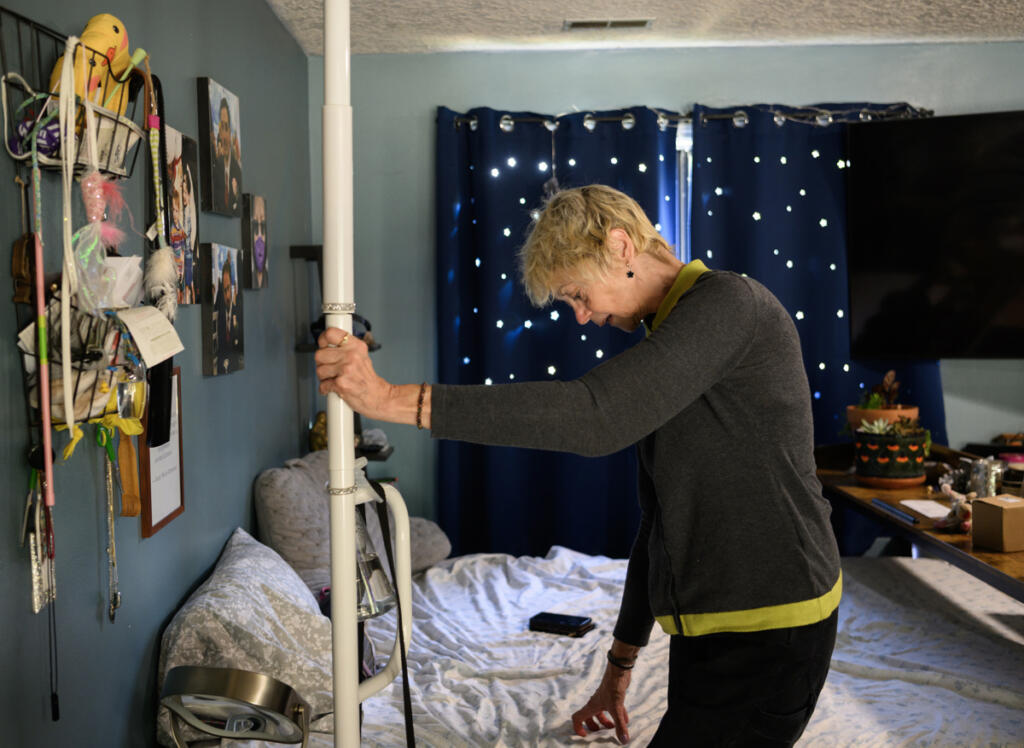 Home care aide Vicki Bickford holds onto a pole to put shoes on Tuesday at her home in Vancouver. This month, the state launched WA Cares, a first-in-the-nation public long-term care benefit. Bickford and other advocates say WA Cares fills a gap in long-term care not covered by Medicare or other forms of health insurance. (Photos by Taylor Balkom/The Columbian)