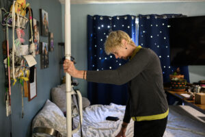 Home care aide Vicki Bickford holds onto a pole to put shoes on Tuesday at her home in Vancouver. This month, the state launched WA Cares, a first-in-the-nation public long-term care benefit. Bickford and other advocates say WA Cares fills a gap in long-term care not covered by Medicare or other forms of health insurance. (Photos by Taylor Balkom/The Columbian)