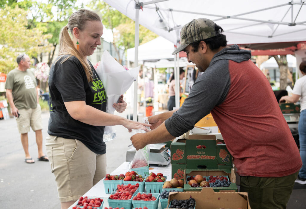 Camas Farmers Market Manager Leah Nichelson, left, buys raspberries from Izzy Rodriguez of Pheasant&rsquo;s Eye Farm on July 22 at the Camas Farmers Market. Nichelson will become the new Downtown Camas Association executive director after current director Carrie Schulstad steps down later this year. (Taylor Balkom/The Columbian)