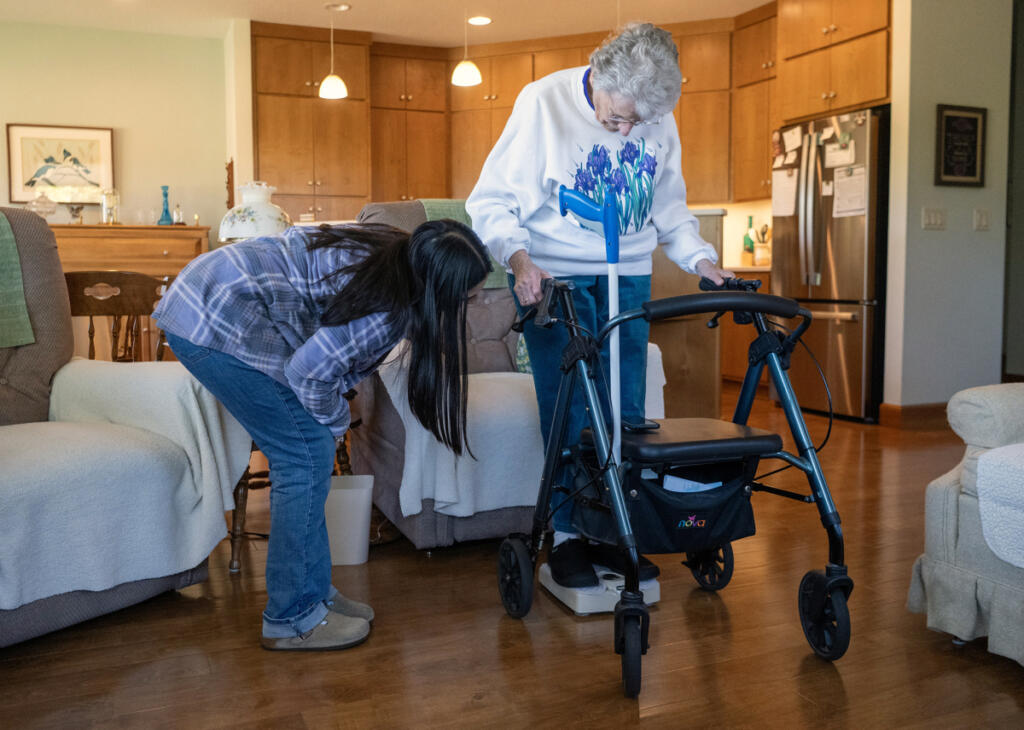 Home Instead caregiver Andrea Salinas, left, checks client Betty Tribe&rsquo;s weight on July 30 at Tribe&rsquo;s home in Ridgefield. (Photos by Taylor Balkom/The Columbian)