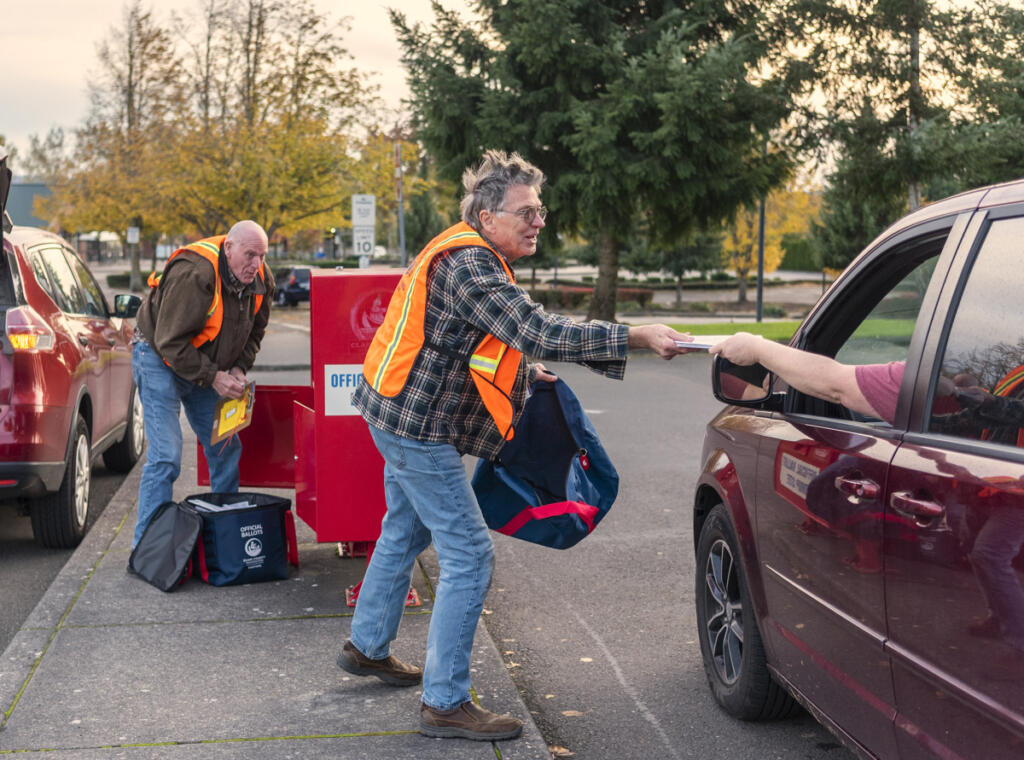 Clark County elections worker Greg Gray, right, takes a ballot from a voter while fellow worker Greg Talbert, left, empties the full ballot drop box into a ballot bag Nov. 8, 2022, at the Fisher&rsquo;s Landing Transit Center. (Amanda Cowan/The Columbian files)