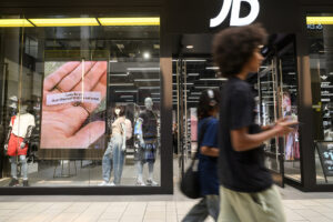 Shoppers walk in front of JD Sports on Aug. 25 at Vancouver Mall. At top, backpacks and other clothing items hang inside JD Sports. (Photos by Taylor Balkom/The Columbian)