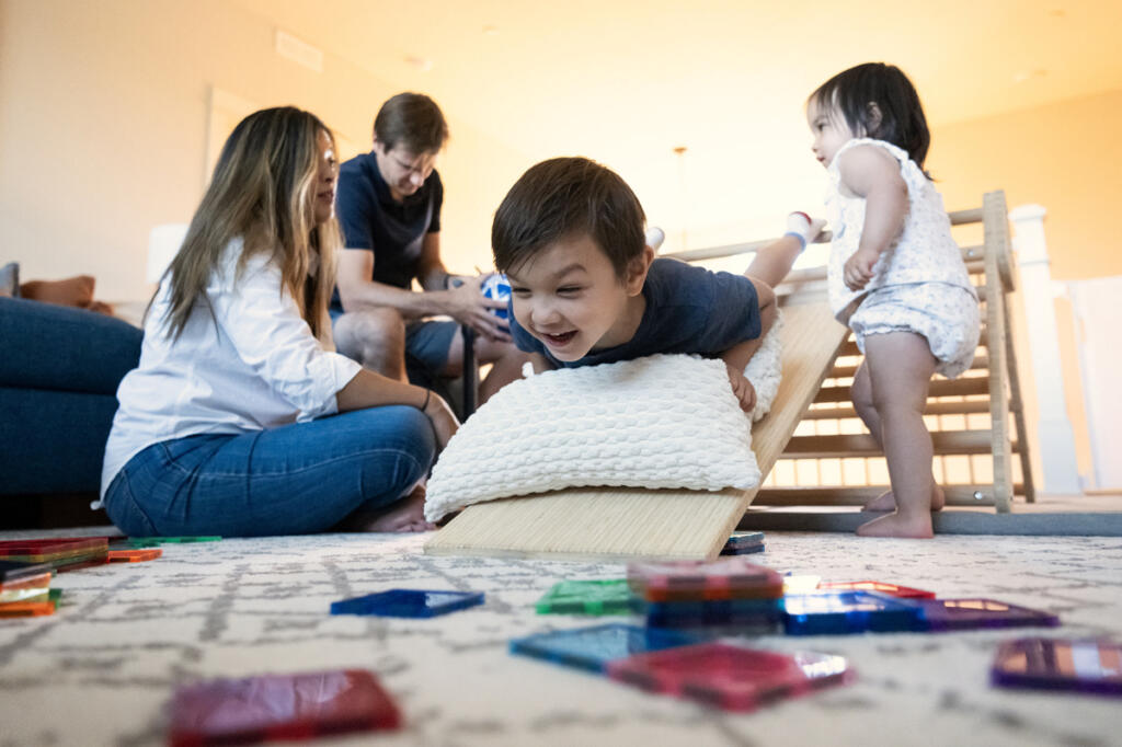 At right, Theodore Wiener, 5, center, slides down a small slide while his family hangs out at their home in Camas.