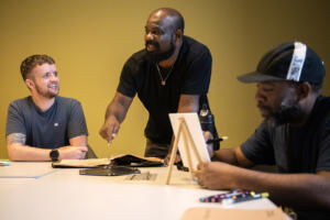 Eliot Reid, from left, laughs Sept. 3 while talking with Gentle Strength Project founder David Bradley as Prince Polk paints during a Gentle Strength Project paint night at Vancouver Community Library. The Gentle Strength Project promotes friendships between men and encourages discussing mental heath. (Photos by Taylor Balkom/The Columbian)