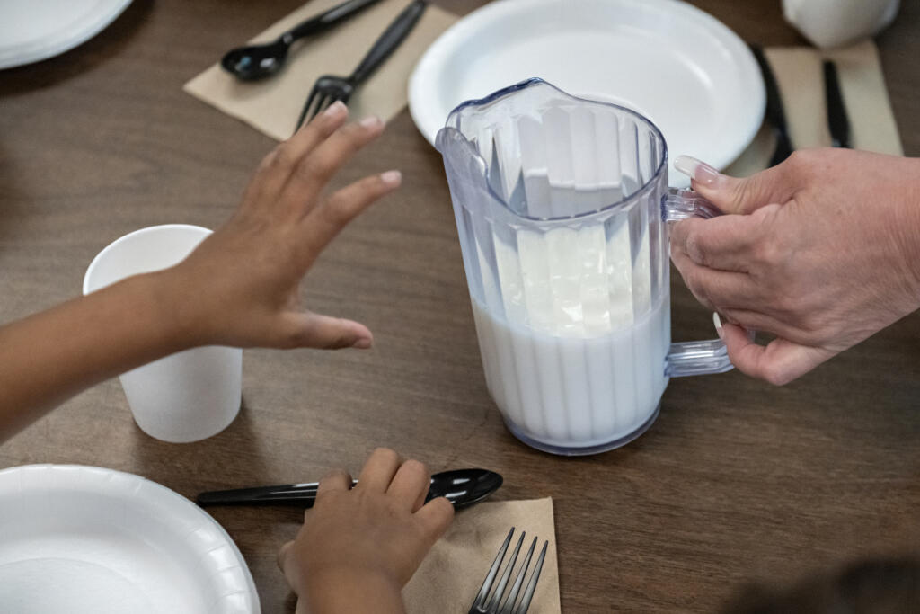 A child reaches out for help with pouring a glass of milk during lunchtime at the Battle Ground Early Learning Center on Monday morning. (Amanda Cowan/The Columbian)