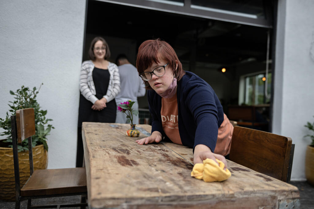 Job coach Jennifer Trout, left, looks on as Daria Eremenko of Washougal keeps the tables at Radiate Coffee and Community in top shape on the morning of Sept. 30. Eremenko said she enjoys the variety of tasks she can do and loves meeting customers. (Amanda Cowan/The Columbian)