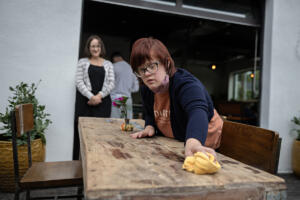 Job coach Jennifer Trout, left, looks on as Daria Eremenko of Washougal keeps the tables at Radiate Coffee and Community in top shape on the morning of Sept. 30. Eremenko said she enjoys the variety of tasks she can do and loves meeting customers. (Amanda Cowan/The Columbian)