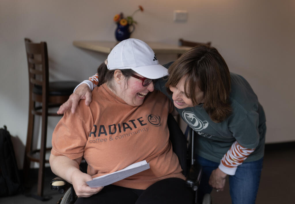 Emily Glenn, left, of Vancouver shares a welcome hug with Kelly Wigen, co-owner of Radiate Coffee and Community in Camas, a new neighborhood coffee shop that opened in September. Glenn was reporting for work on a recent Wednesday morning. The business provides inclusive employment for people with disabilities. (Amanda Cowan/The Columbian)