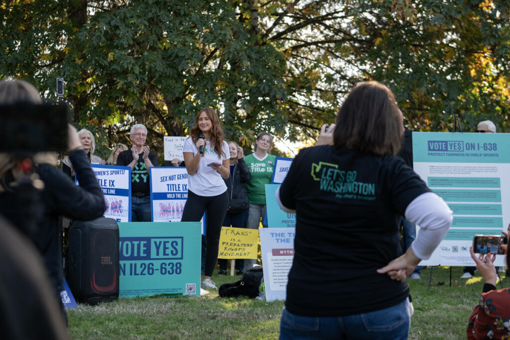 Speaker Frances Staudt, with microphone, joins protesters outside Wednesday&rsquo;s 4A Greater St. Helens League district cross country championship in Camas, where a transgender girl competed. Staudt received national attention two years ago when she walked off the basketball court rather than play against a team with a transgender player. (Amanda Cowan/The Columbian)